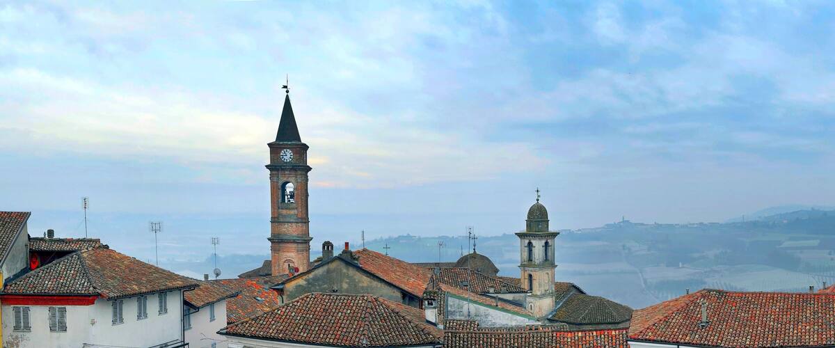 A town with red-tiled roofs, a prominent clock tower, and a distant view of rolling hills.