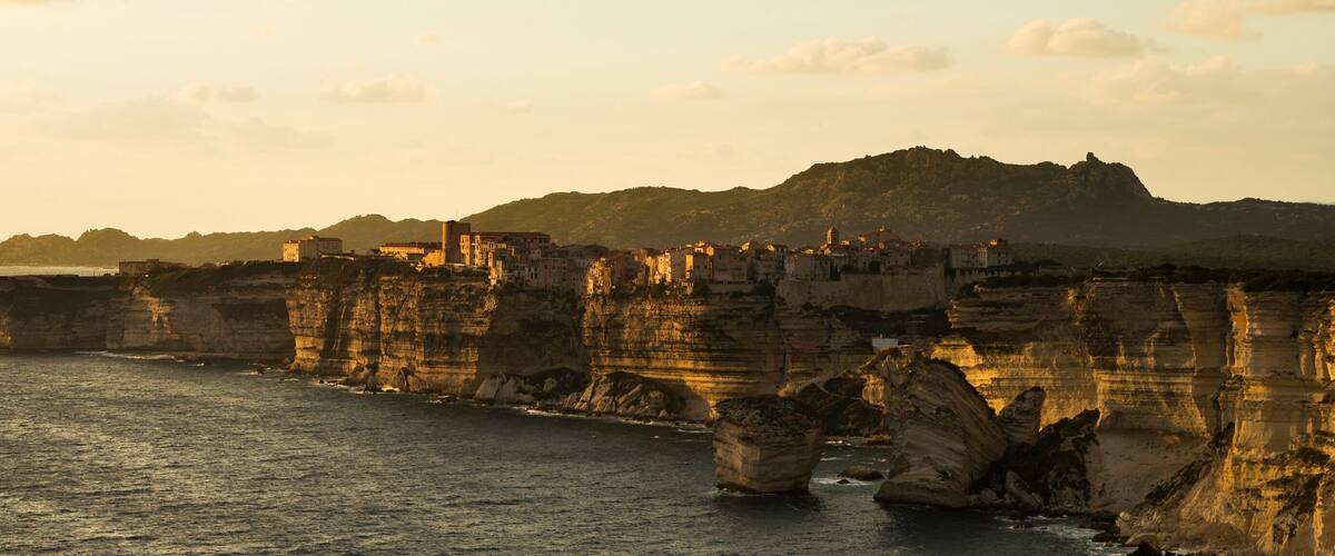 A coastal landscape with prominent rock formations and a distant mountain range.