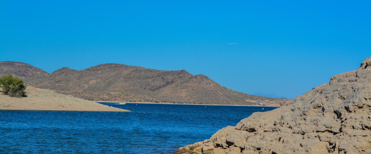 A coastal landscape with a clear blue sky, rocky terrain, and a calm sea.
