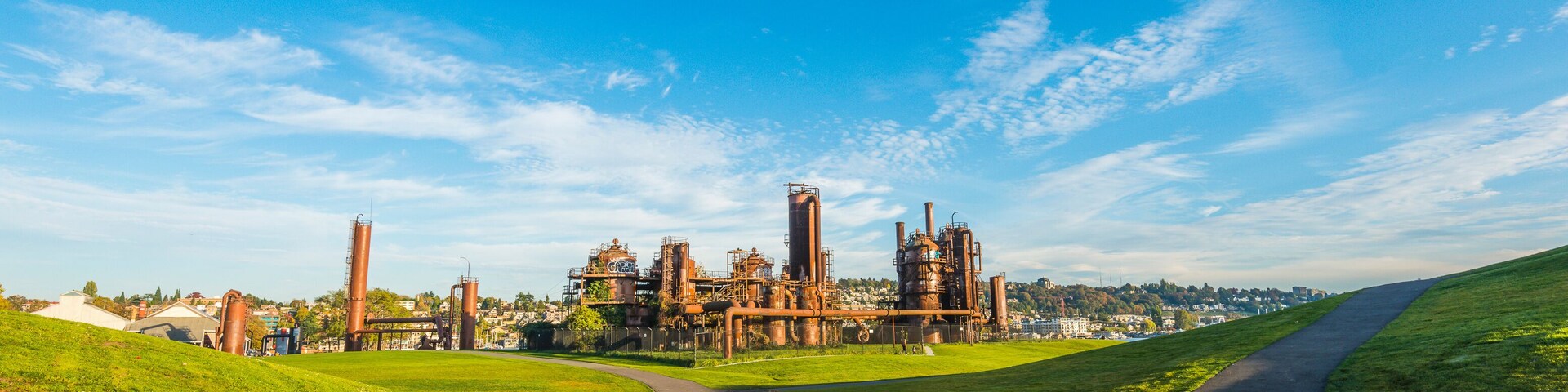 Un camino que lleva a un complejo industrial con grandes estructuras y un cielo azul claro.