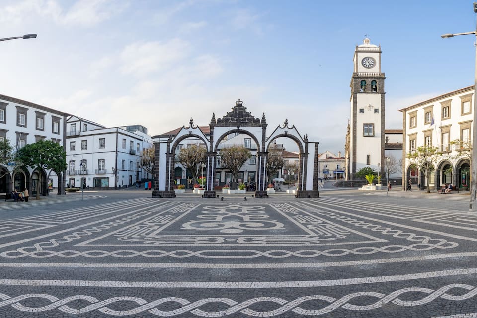 Una plaza con un monumento central, una torre del reloj y edificios circundantes.