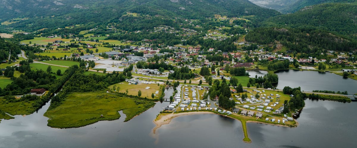 A lakeside town with a marina, surrounded by mountains and greenery.