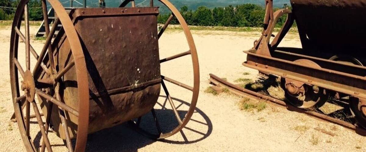 A vintage tractor with large wheels and a wooden structure, set against a backdrop of mountains and clear skies.