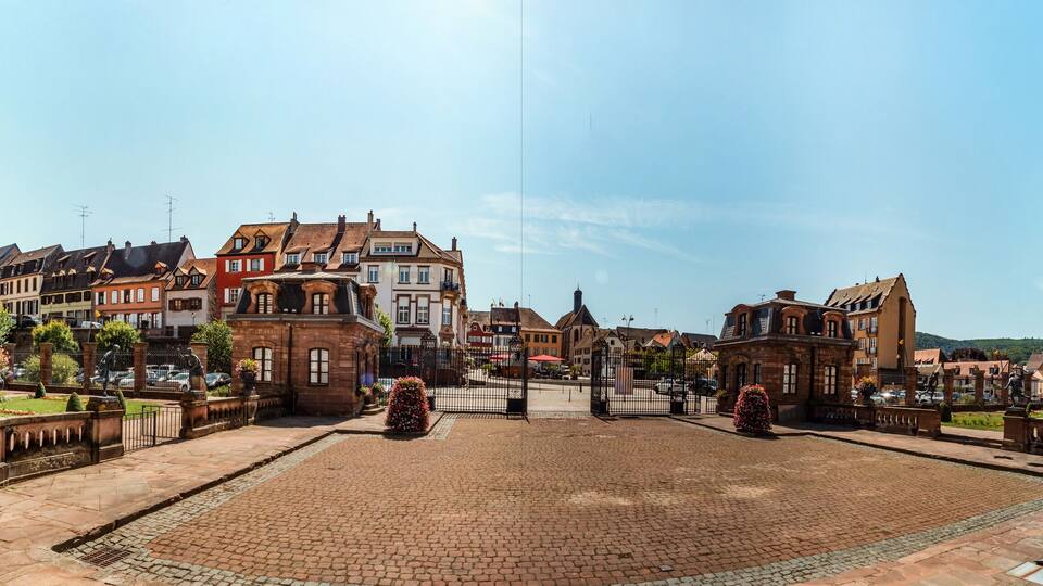 A cobblestone square with statues, historic buildings, and a clear sky.