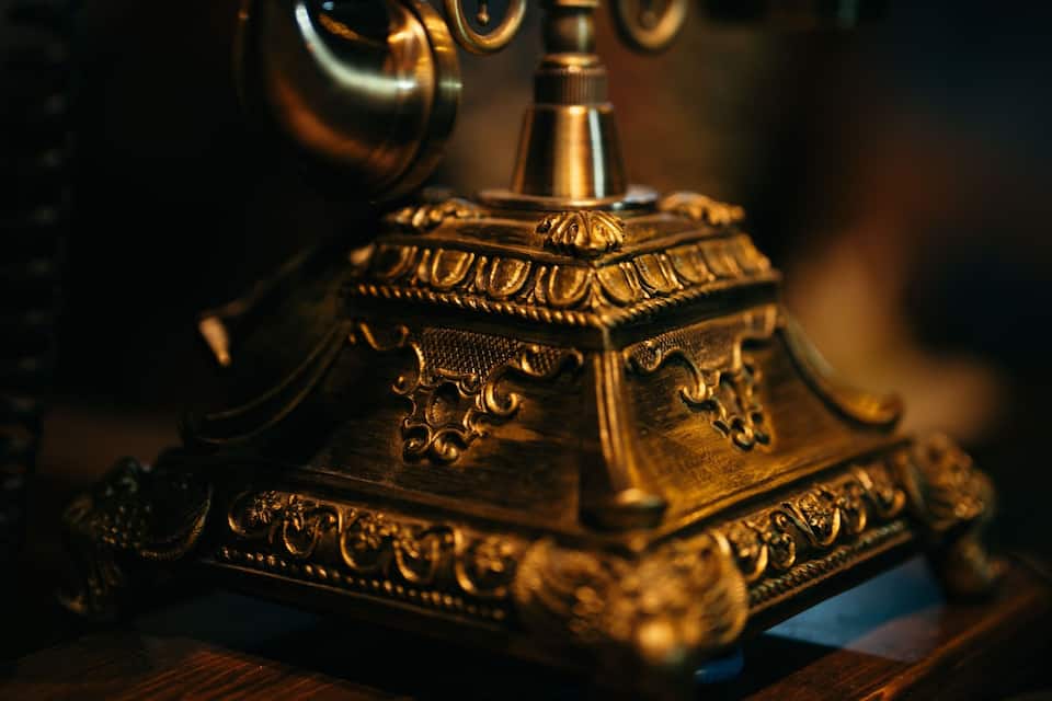 An ornate antique telephone with intricate designs, placed on a wooden surface.