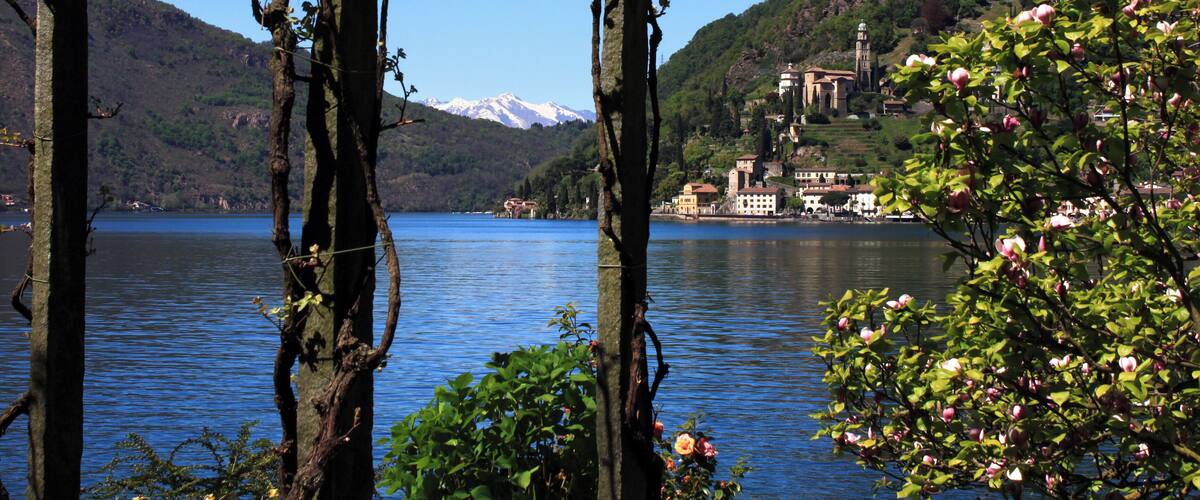 A wooden pergola over a lake with mountains in the background and a church on a hill.