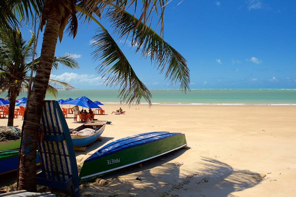 Een strand met palmbomen, blauwe parasols en boten.
