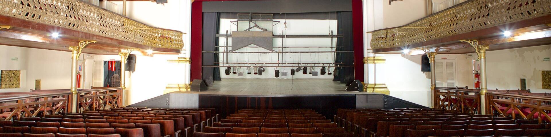 An empty theater with ornate golden railings and a red stage backdrop.