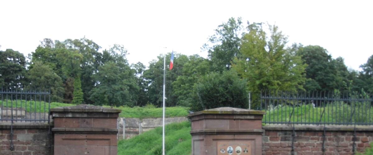A brick gate with a sign, a gravel path, and a flagpole with a flag.