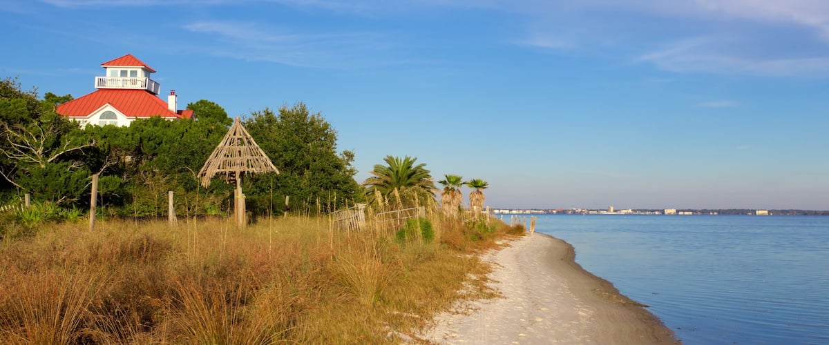 A beach with a red-roofed building, a thatched structure, and palm trees.