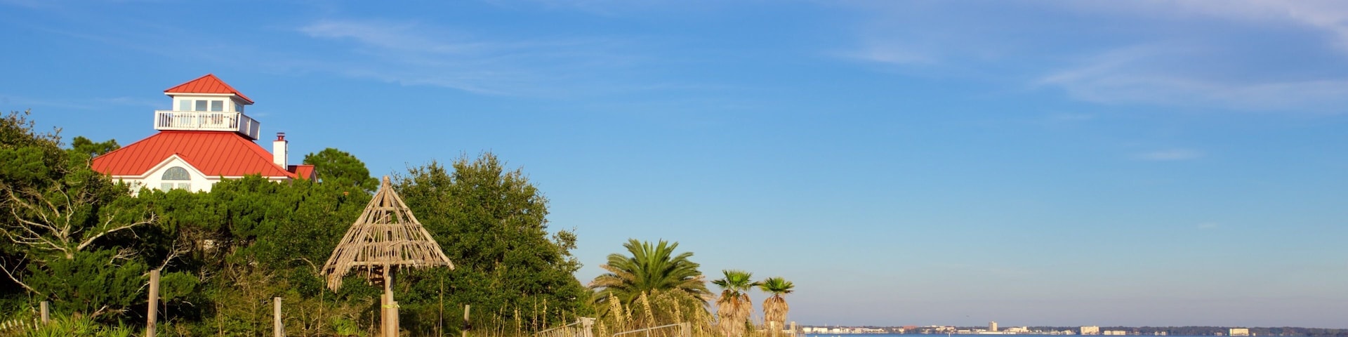 A beach with a red-roofed building, a thatched structure, and palm trees.