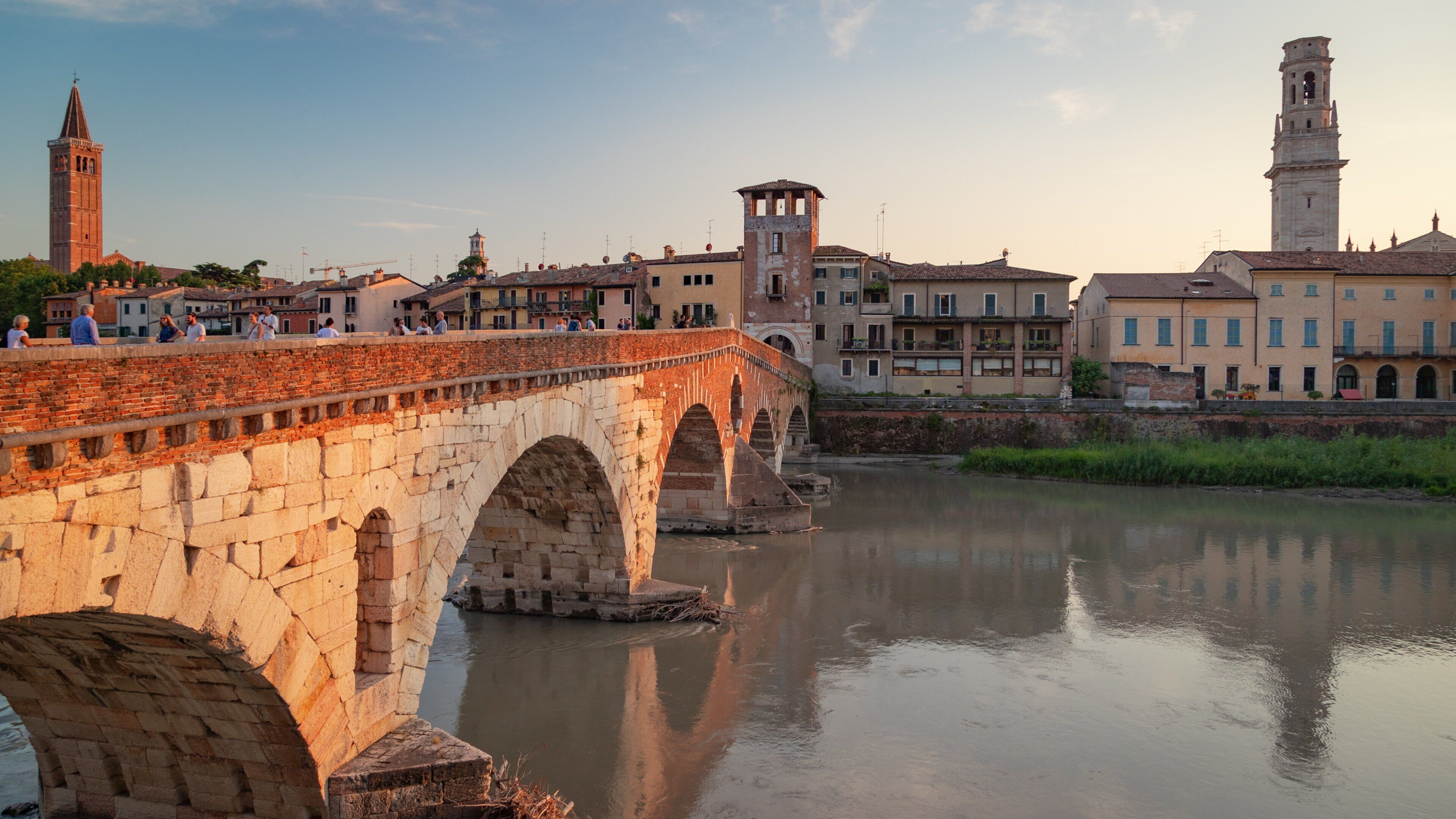 A stone bridge over a river with historic buildings and towers in the background.
