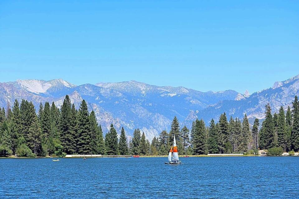 Ein See mit einem Segelboot, umgeben von dichten Wäldern und schneebedeckten Bergen.