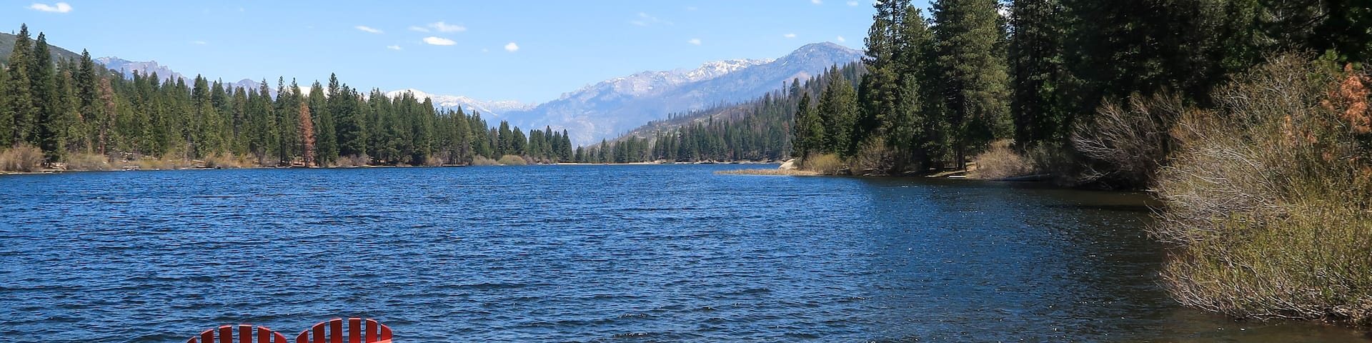 A lake with a red bench, surrounded by trees and mountains in the background.