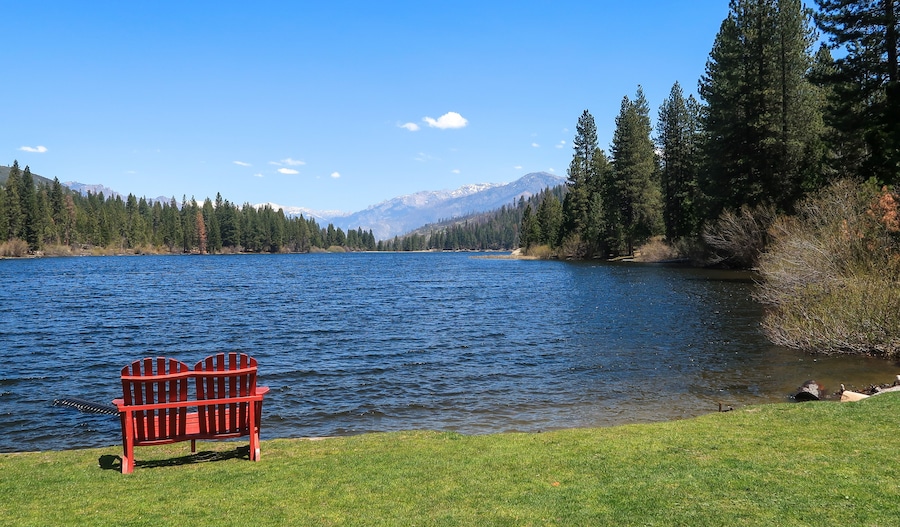 A lake with a red bench, surrounded by trees and mountains in the background.
