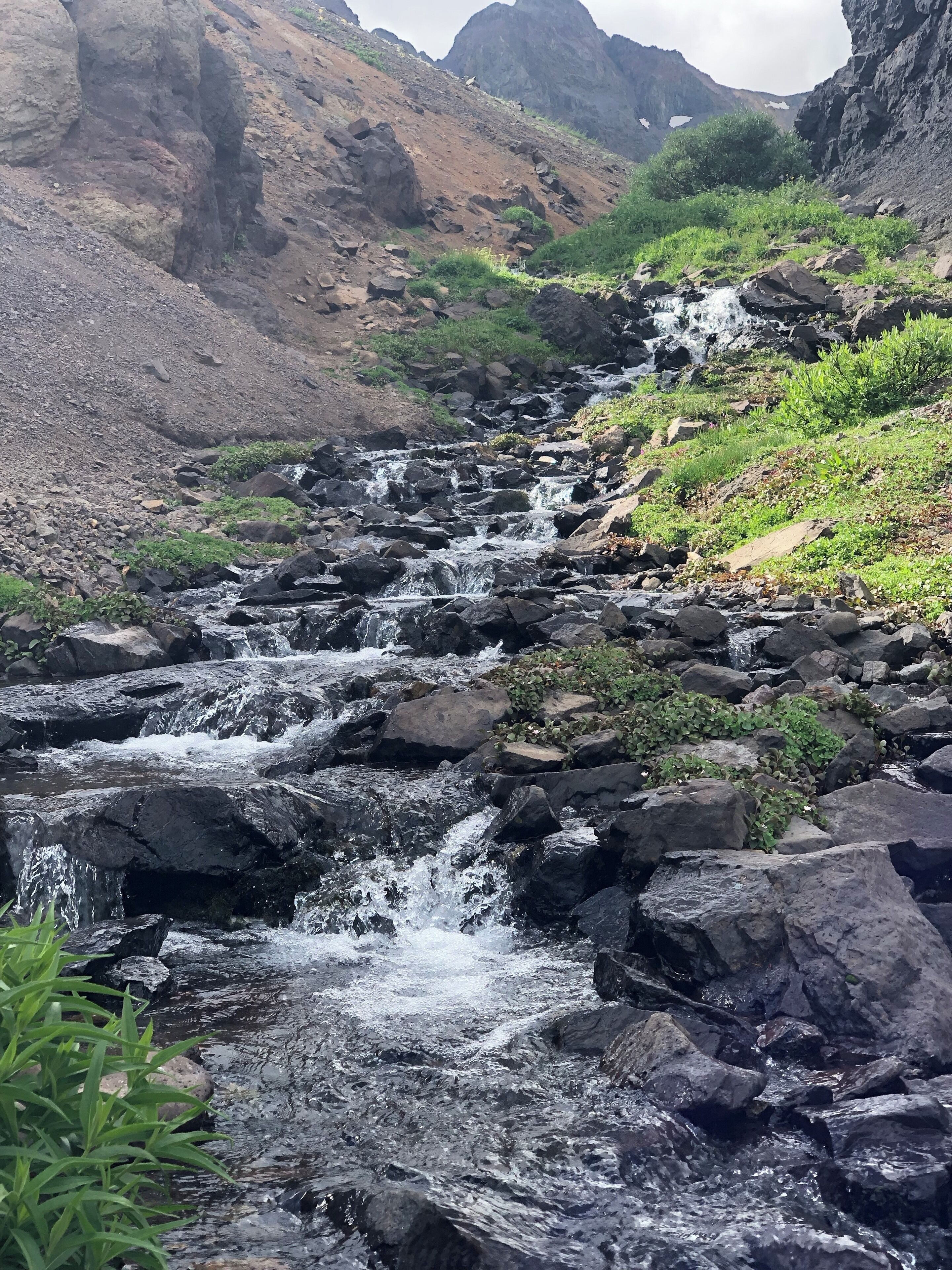 A rocky stream flowing through a mountainous landscape with patches of greenery.