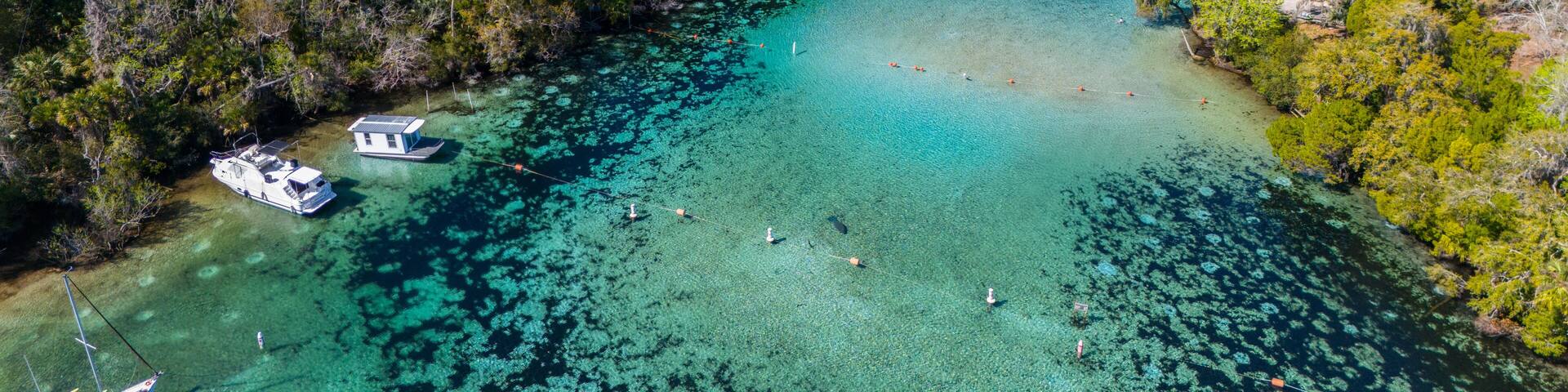 An aerial view of a turquoise lagoon surrounded by dense forest, with a small houseboat docked near the shore.
