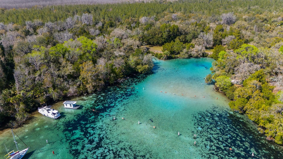 An aerial view of a turquoise lagoon surrounded by dense forest, with a small houseboat docked near the shore.
