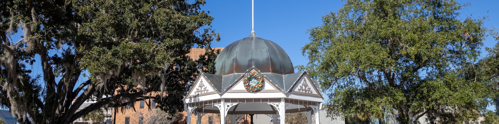 A gazebo with a dome, surrounded by a white fence, and adorned with wreaths.