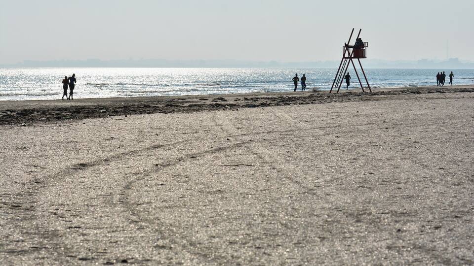A beach with footprints, a lifeguard tower, and people walking along the shore.
