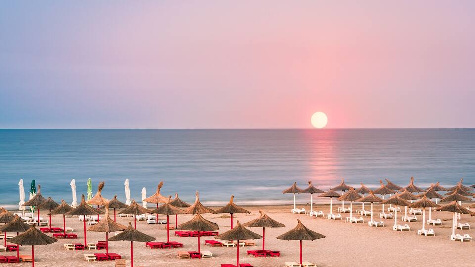A beach with rows of sun umbrellas and lounge chairs.