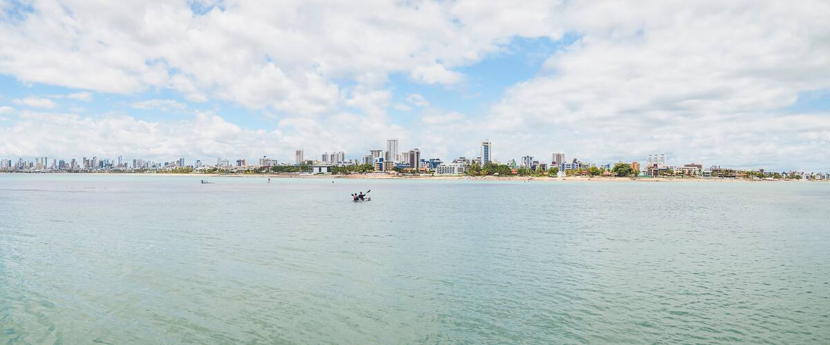 Panoramic view of Praia do Bessa beach and the city of Joao Pessoa. Seafront buildings, some tourists riding kayak and stand up paddle.
