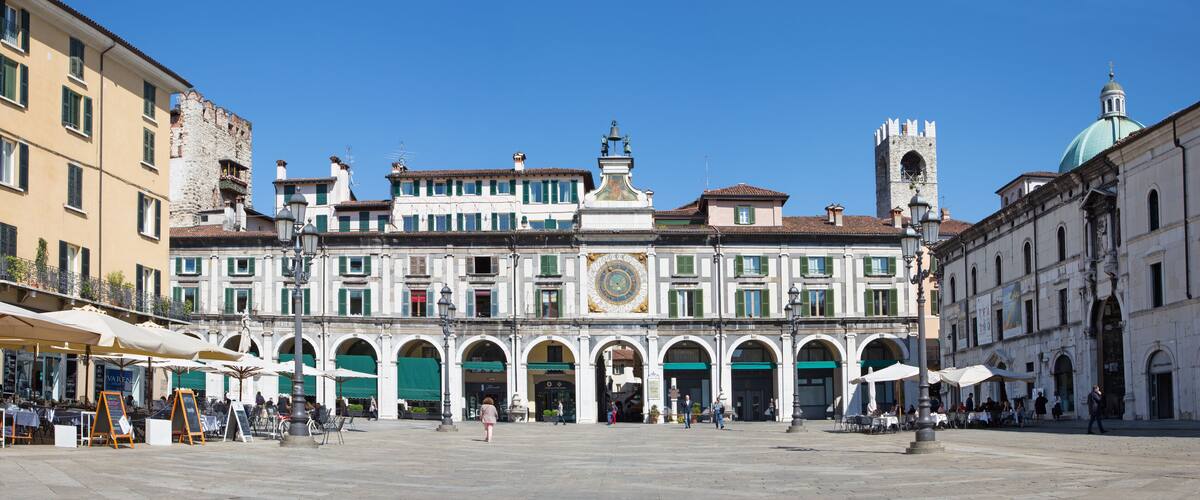 A historic square with a prominent clock tower, a fountain, and a large open plaza with cafes.