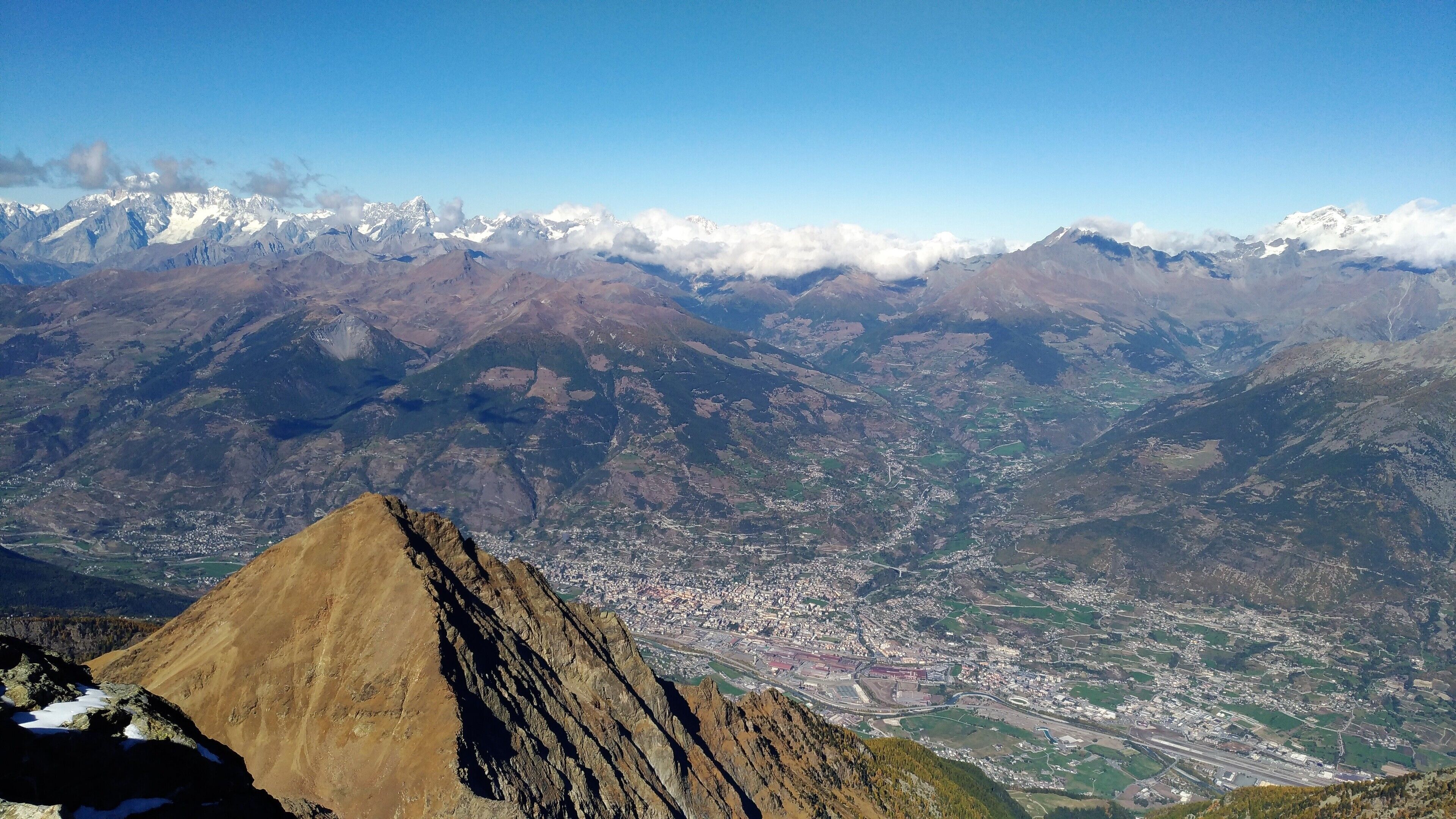 A mountain range with a prominent peak in the foreground and a valley with a town below.