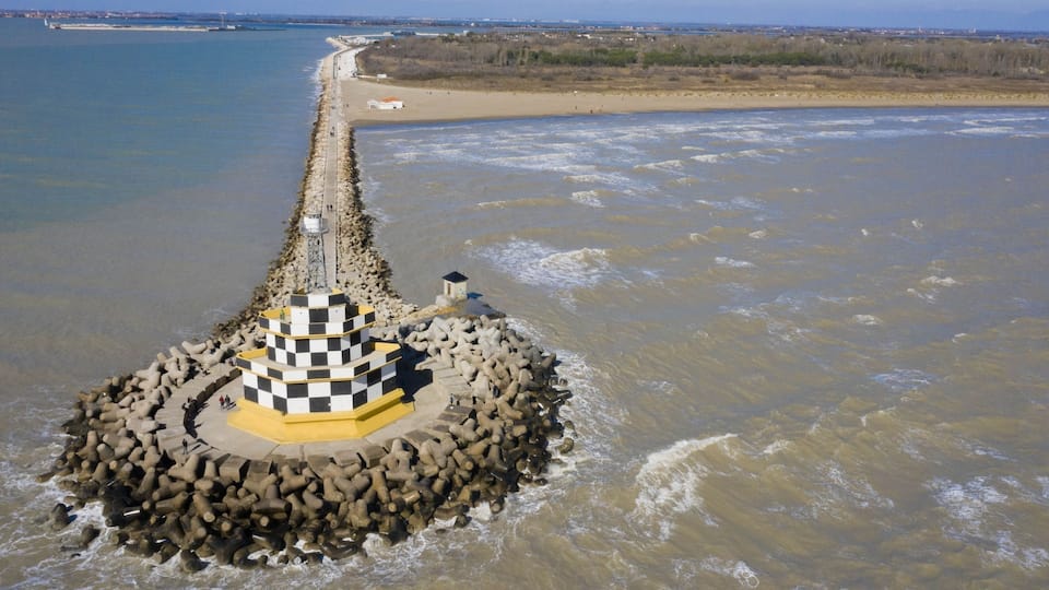A lighthouse on a rocky breakwater with a beach in the background.