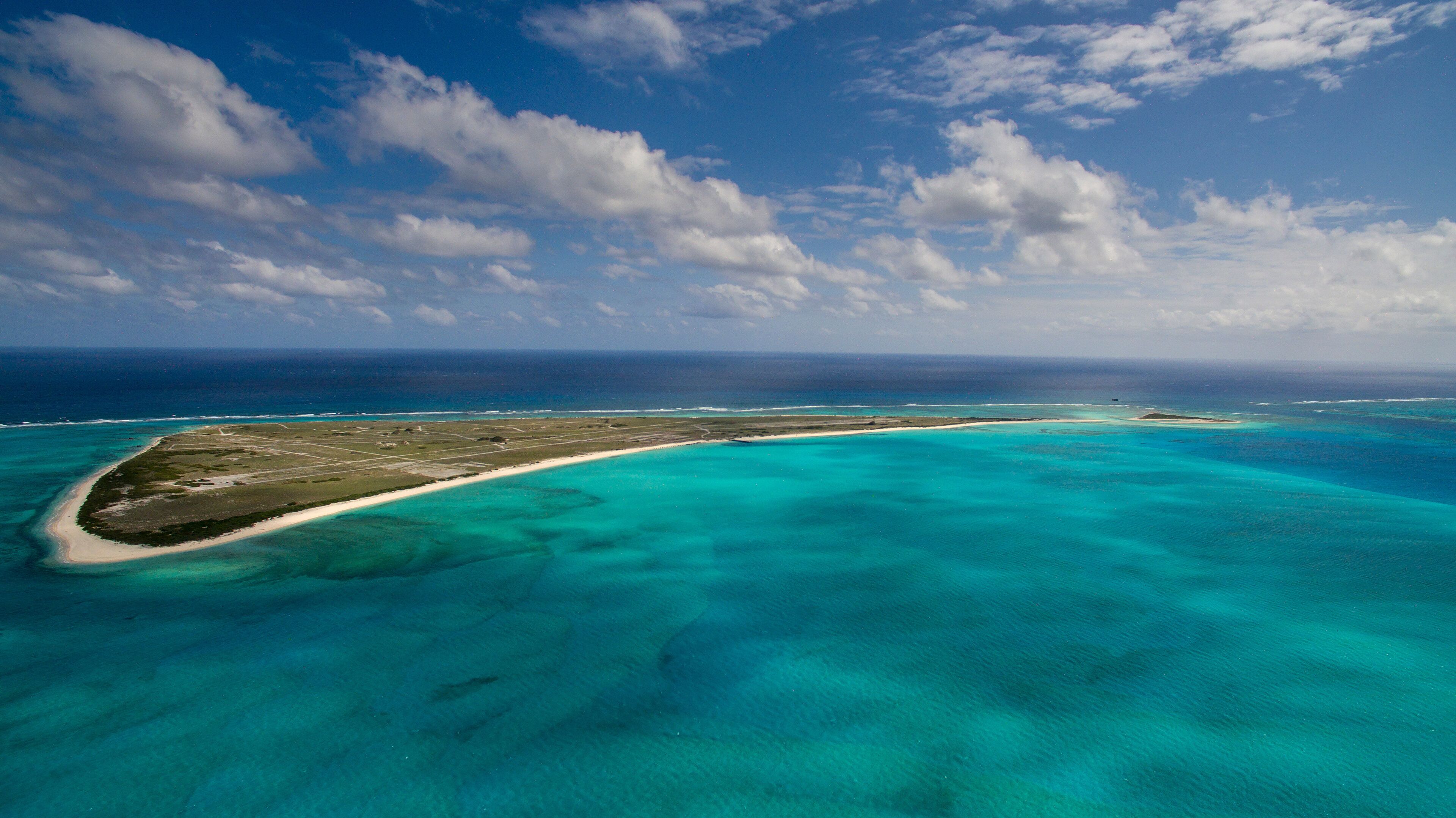 An aerial view of a turquoise island with clear waters and a sandy beach.