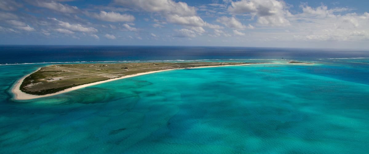 An aerial view of a turquoise island with clear waters and a sandy beach.