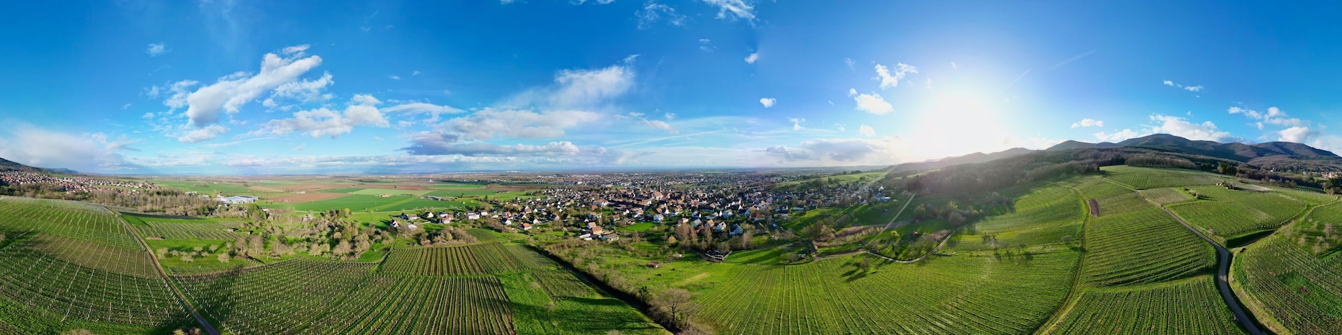 360 panorama aerial drone view above the Uffholtz and Wattwiller villages green vineyard hills in a Alsatian valley by sunny day with blue sky, dark stormy clouds in the distance, with paths