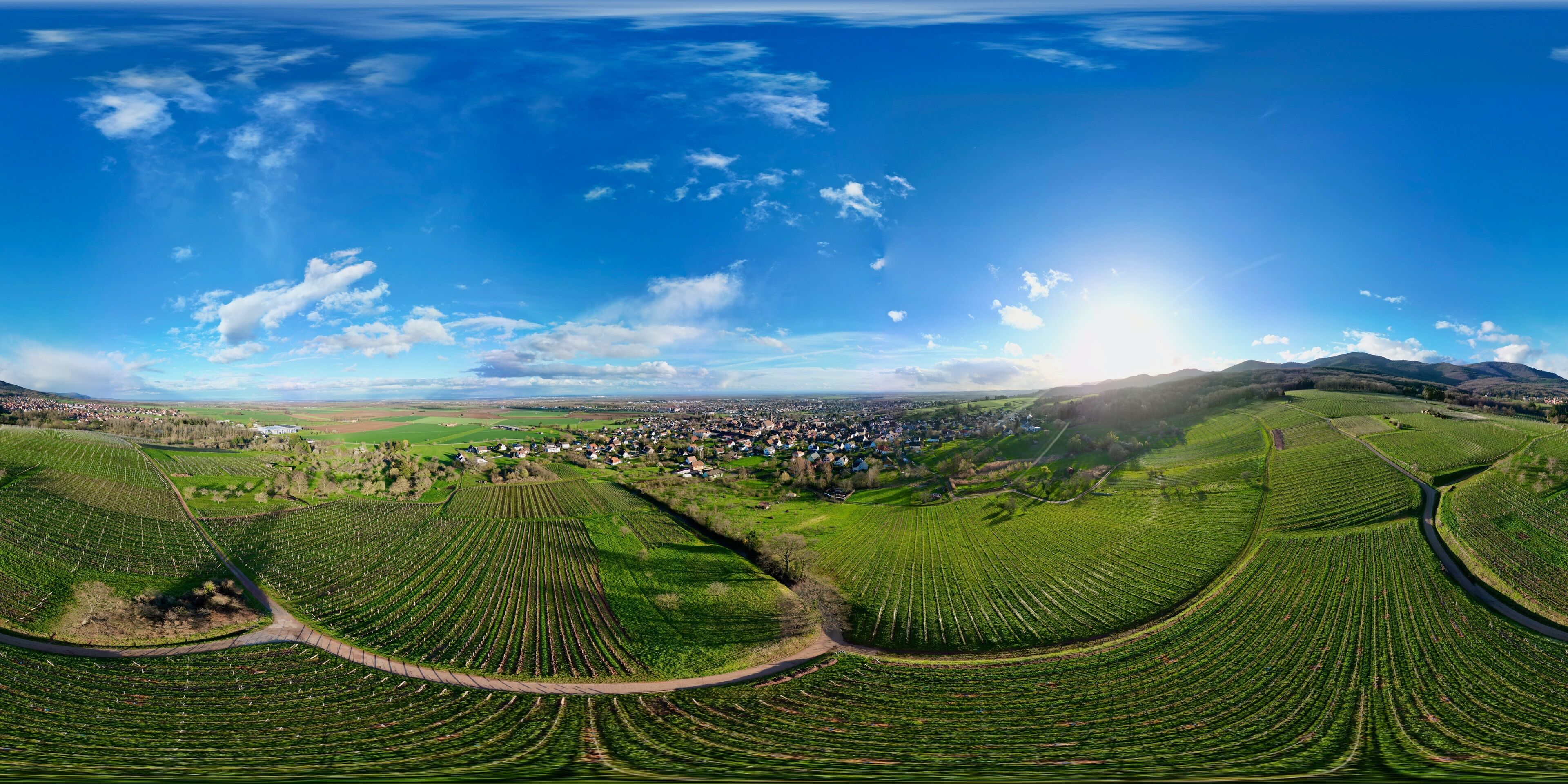 A panoramic view of a rural landscape with terraced fields, a small town, and rolling hills under a clear sky.