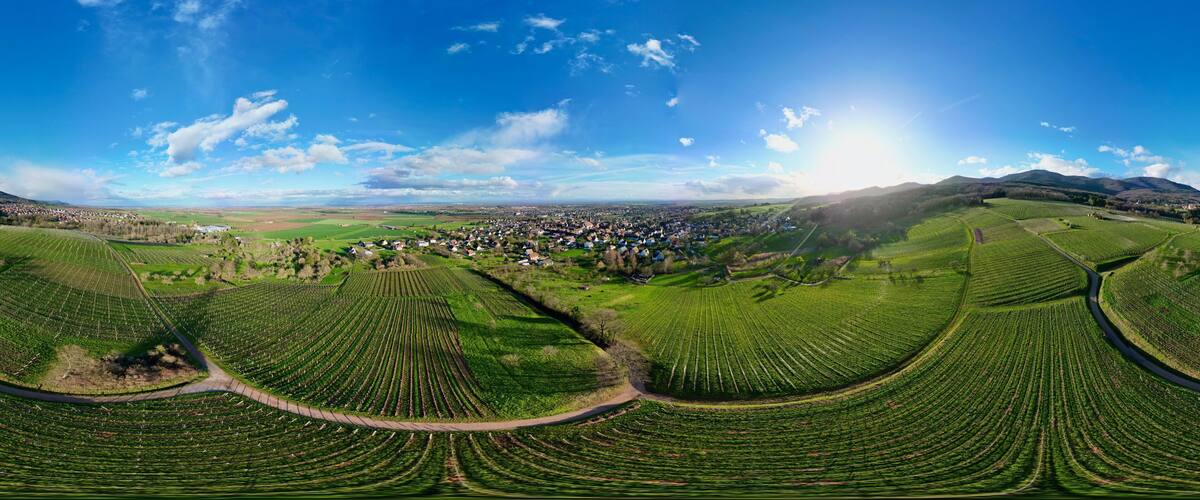 A panoramic view of a rural landscape with terraced fields, a small town, and rolling hills under a clear sky.