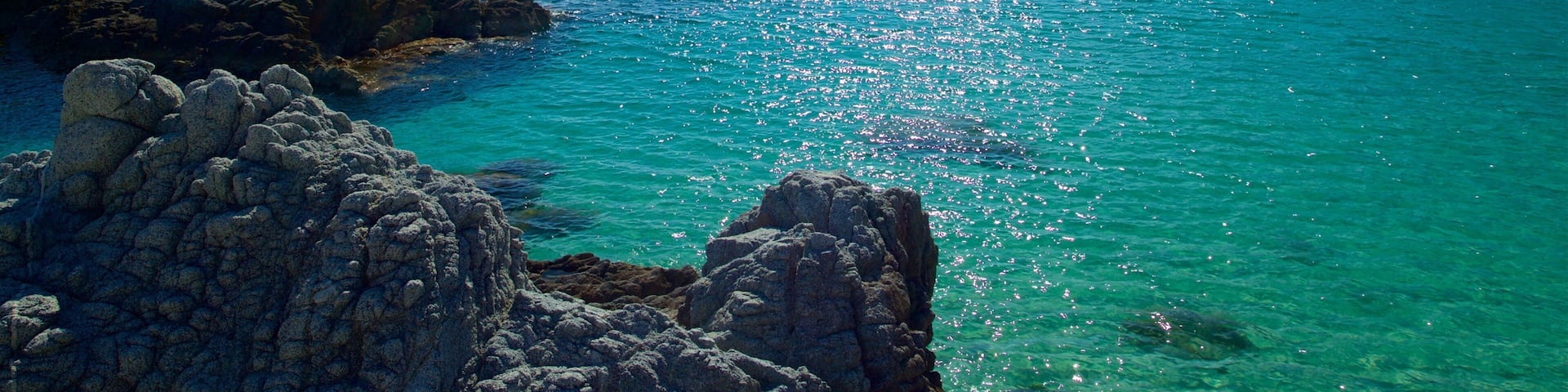 A coastal landscape with clear turquoise waters, rocky formations, and a distant mountain range.