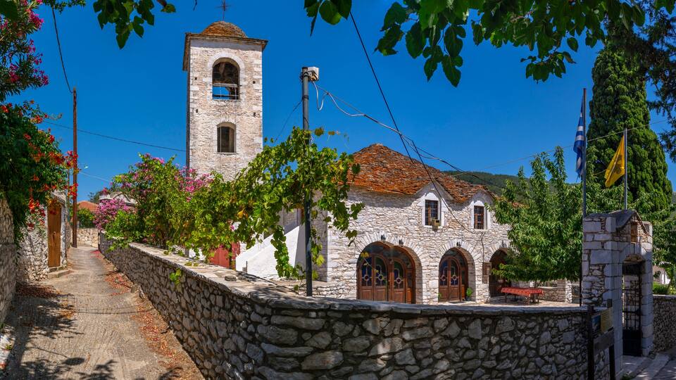 A stone church with a bell tower, surrounded by trees and a stone wall.