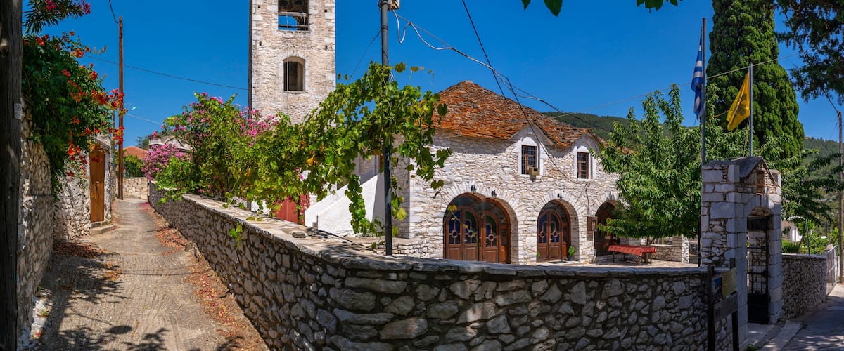 A stone church with a bell tower, surrounded by trees and a stone wall.