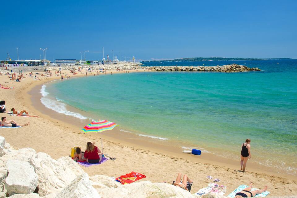 Een zandstrand met helder turquoise water, rotsachtige rotsformaties en enkele parasols.