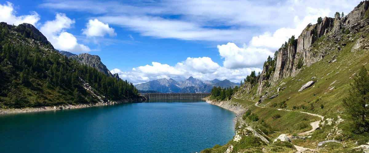 A lake surrounded by mountains, a clear sky, and a distant dam.