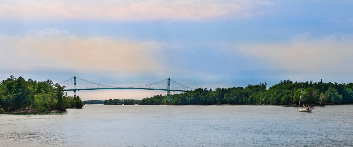 A suspension bridge over a calm river, surrounded by dense forest.
