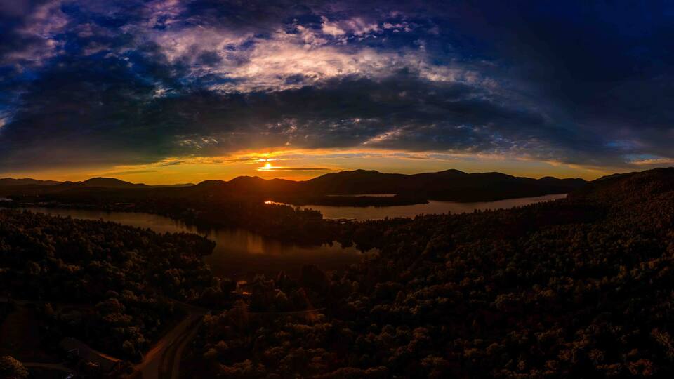 A sunset over a mountainous landscape with a lake and forested areas.