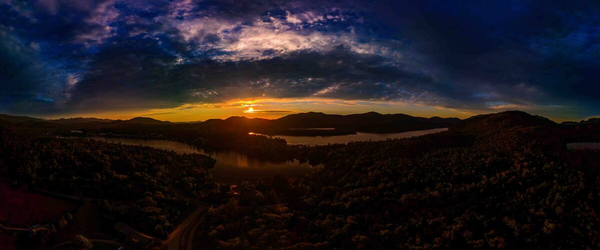 A sunset over a mountainous landscape with a lake and forested areas.