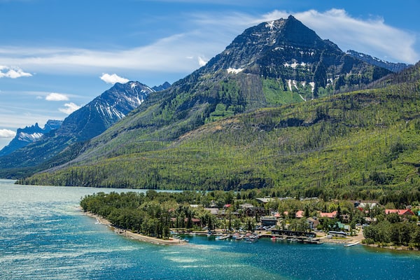 A mountain top called the Bears Hump at Waterton Lakes National Park, Canada. It is a beautiful, colorful mountain with a rainbow, blue sky, and clouds.