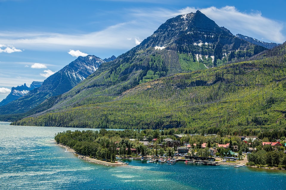 A lake surrounded by mountains, a small town with houses and boats, and a clear sky.