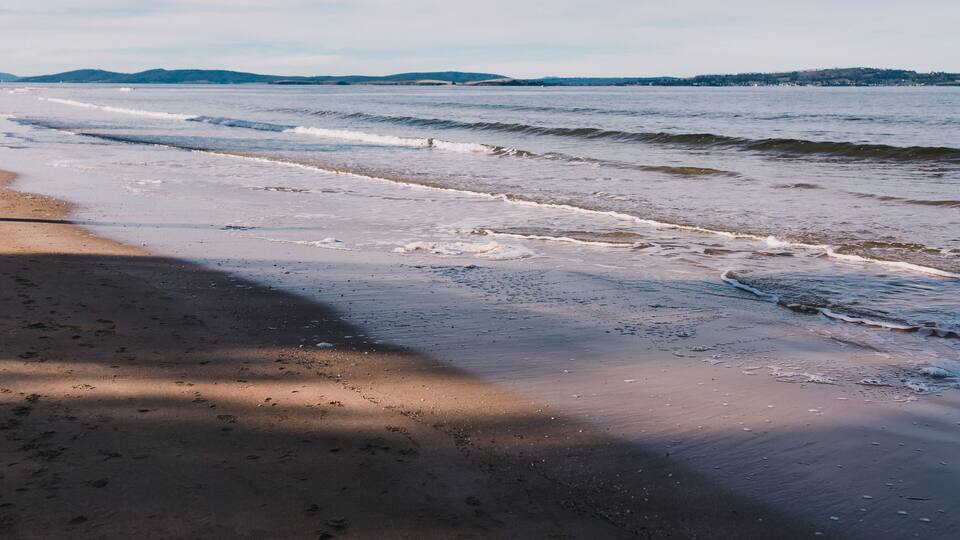 A beach with waves, a sandy shore, and distant hills.