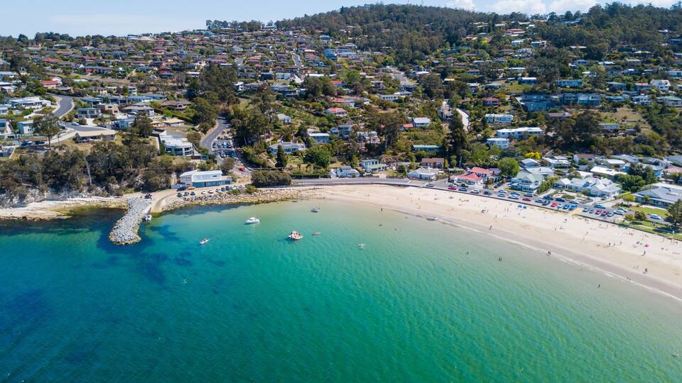 A coastal town with a beach, clear turquoise waters, and residential buildings.