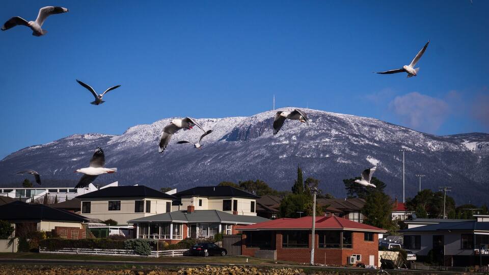A mountain with snow-capped peaks, houses, and a body of water.