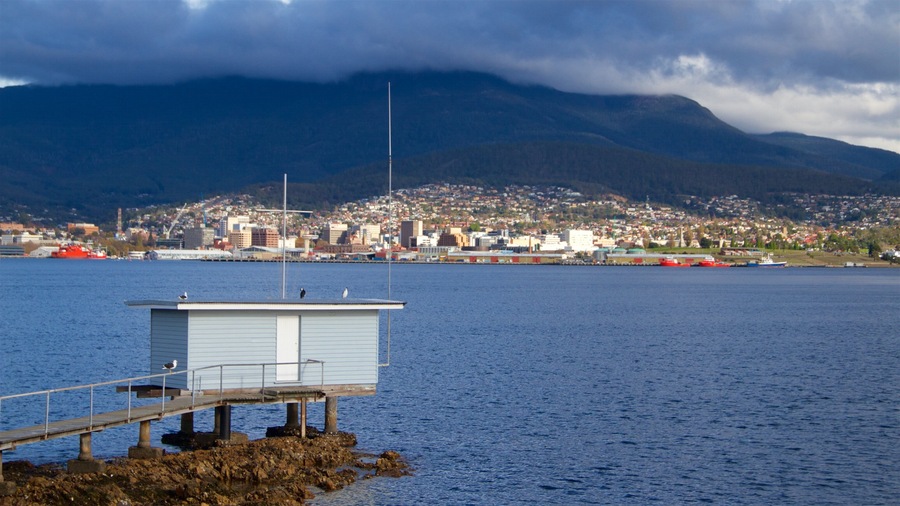 A coastal city with a dock, a lighthouse, and mountains in the background.