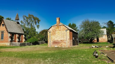 Un paysage rural avec une grange en briques, une structure en bois dotée d’un toit en pente et un espace clos où se trouvent des canards.