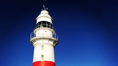 A tall white and red lighthouse with a small house nearby.